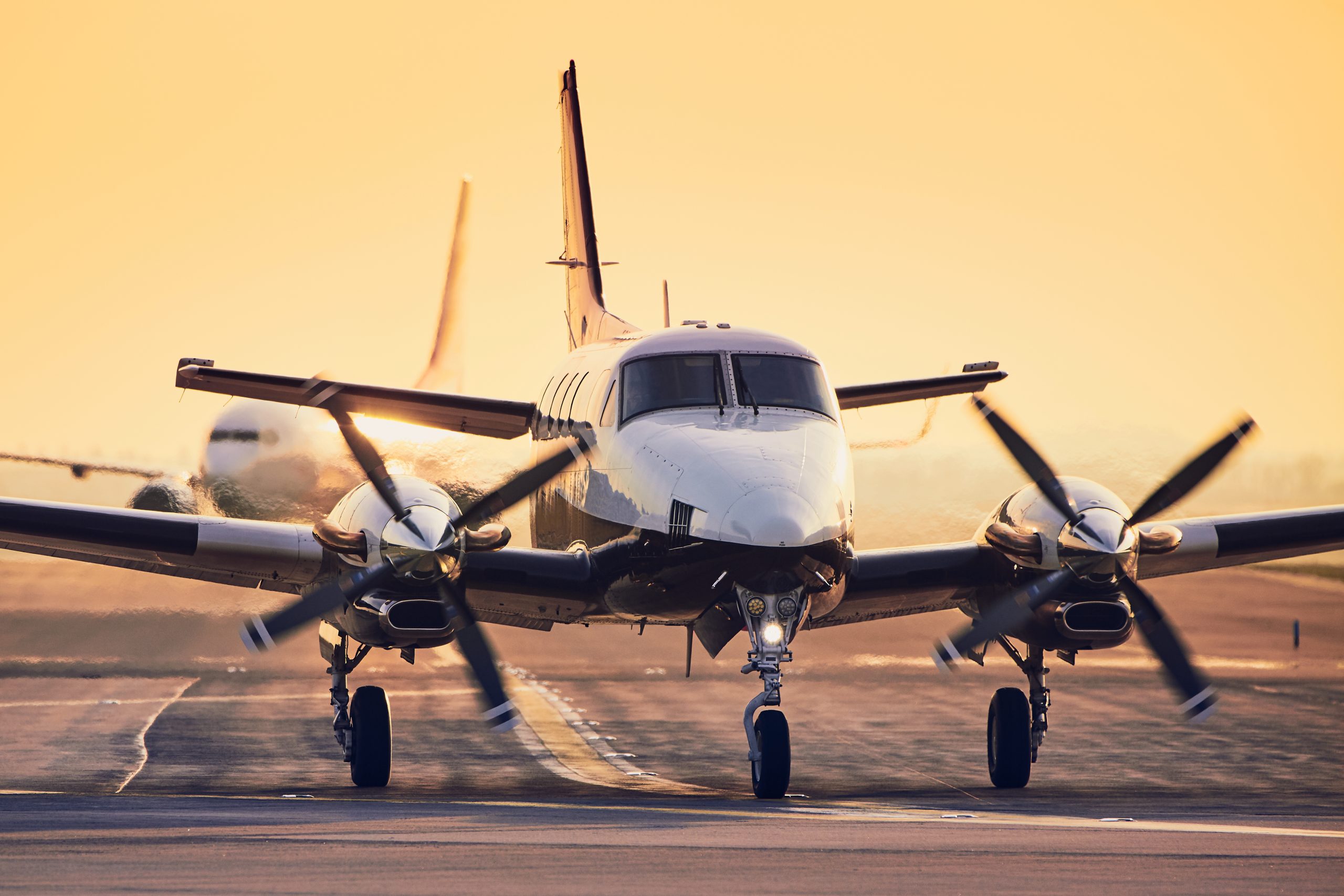 Modern propeller plane against commercial airplane on runway. Traffic at airport during sunset.